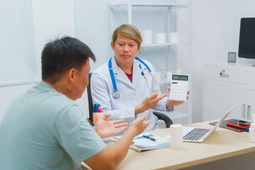 Asian male doctor specializing in cardiology explains heart disease to a patient using a heart...