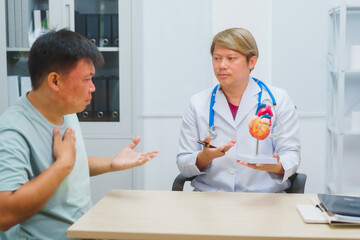 Asian male doctor specializing in cardiology explains heart disease to a patient using a heart model. He provides expert advice, discusses symptoms, risk factors, and treatment in a modern clinic.