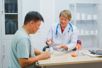 Asian male doctor specializing in cardiology explains heart disease to a patient using a heart...