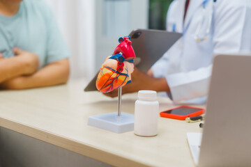 Asian male doctor specializing in cardiology explains heart disease to a patient using a heart...