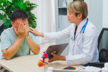 Asian male doctor specializing in cardiology explains heart disease to a patient using a heart...
