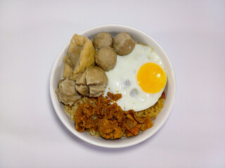 A bowl of Indonesian instant noodles (Indomie) topped with meatballs, fried tofu, fried egg, and a spicy, crispy topping. Represents Indonesian cuisine, instant noodles, comfort food, quick meals