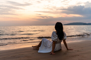 Lonely young woman sitting and watching the beautiful sunset on tranquil beach