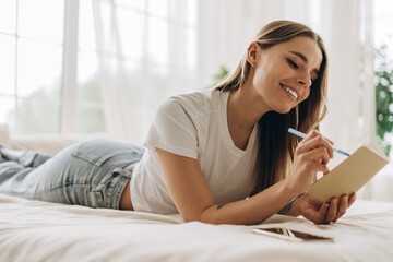 Young beautiful woman writing on notebook while lying on bed