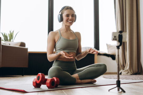 Fitness influencer recording online course wearing headphones and sitting on yoga mat