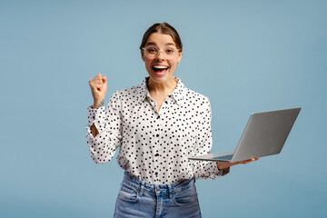 Excited businesswoman celebrating success holding laptop and raising fist