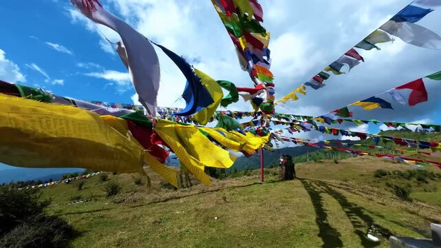 Colorful Tibetan prayer flags flutter in the wind against lush green hills and scenic landscapes of Singalila Ridge, Darjeeling, West Bengal, India in the Indian Himalayas.