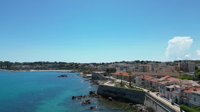 View of the Cote d'Azur featuring the Ch&acirc;teau Grimaldi and Mus&eacute;e Picasso in Antibes, France. Clear blue sky, calm sea, and coastal buildings are visible.