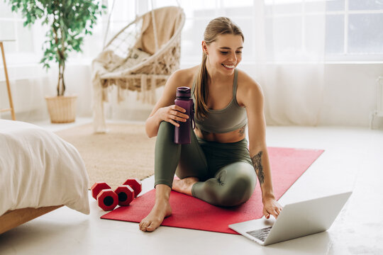 Fitness instructor with tattooed body preparing online workout session using laptop at home