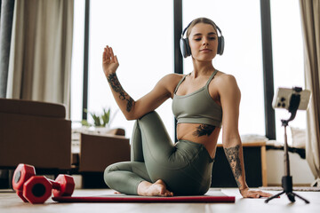 Fitness influencer practicing yoga online using smartphone and headphones