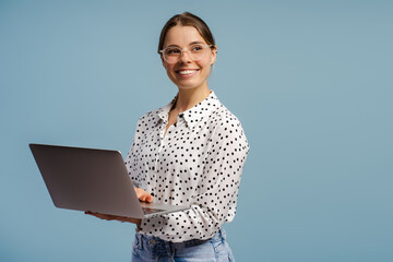 Smiling businesswoman holding laptop and looking away on blue background