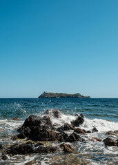 Waves splashing onto the rocky coastline of the northern tip of Cap Corse on the Mediterranean island of  Corsica with the island of Giraglia in the distance
