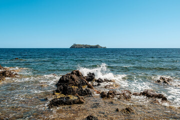 Waves splashing onto the rocky coastline of the northern tip of Cap Corse on the Mediterranean island of  Corsica with the island of Giraglia in the distance