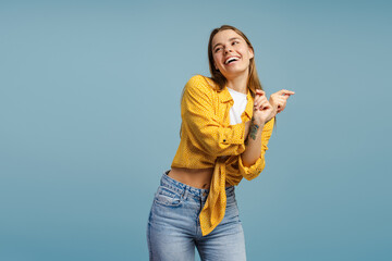 Cheerful young woman in casual clothes dancing looking away on blue background