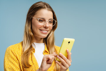 Happy young woman using a smartphone and smiling on a blue background
