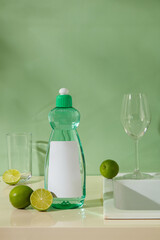 Dish soap bottle and glassware arranged with limes on a green background. The combination suggests fresh and eco-friendly cleaning. Product with ingredient from lime