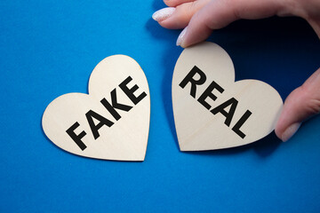Real or Fake symbol. Concept word Real or Fake on wooden hearts. Businessman hand. Beautiful blue...