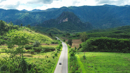 Aerial view of car running on the road among the forest and mountains