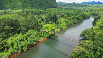 Aerial view of the bridge over the river with the greenery rainforest and mountains