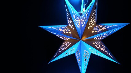 Christmas paper star in blue light on black background. Holiday Paper Decorations.Christmas symbol wallpaper. Glowing festive decor. 4k footage - Powered by Adobe