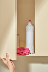 A person reaches into a beige cabinet to reveal a bottle of cleaning solution and a pair of pink...