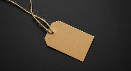 A simple blank brown paper tag hangs from rustic twine against a deep black background. Ideal copy space for text or logos, perfect for showcasing sales, prices, or branding. Use for retail, crafts, g