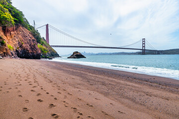 Kirby Cove Beach in California with red sand, blue ocean waves, and dramatic cliffs covered in pine trees. A hidden gem near San Francisco, perfect for nature, travel, and coastal exploration themes