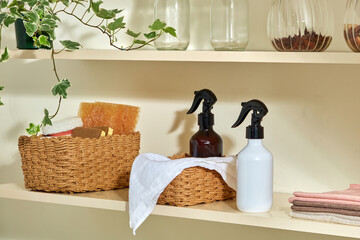Two spray bottles and a white towel in a woven basket next to a glass jar. A decorative and functional cleaning device in a cozy kitchen. Advertising a specialized product for the kitchen