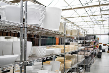 A collection of flowerpots displayed on shelves inside of a plant shop, showing variety in shape and size.