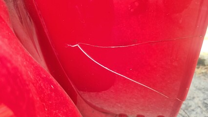 Depict visible damage to the red body of a motorbike or scooter sharp crack on the painted surface....