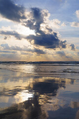At sunset on the beach, the sun sets behind the clouds, reflecting vibrant colors over the sea on the coast, City of Donostia-San Sebastian.
