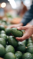 A person selecting a ripe avocado from a pile at a market or grocery store with a blurred background.