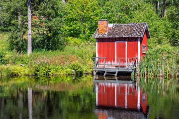 Idyllic Red wooden cottage on the lakeshore in the forest with reflections in the water
