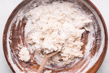 Overhead view of bread dough being mixed in a wooden bowl, top view of homemade bread dough in a...