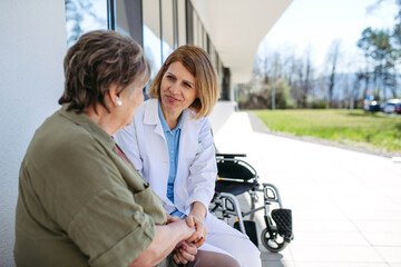 Doctor and elderly patient sitting in front of hospital building and talking.