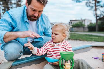 Father and little toddler son playing in the sandbox on playground.
