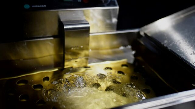Industrial deep fryer with tortilla or flatbread floating in oil, golden reflections on metal.