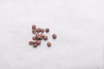 Overhead view of dark chocolate chips on a white countertop, top view of chocolate chips on a white background