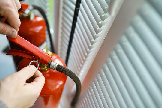 hand presses the trigger fire extinguisher available in fire emergencies conflagration damage background. Safety