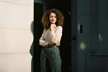 Smiling african american businesswoman wearing white blouse standing with arms crossed against marble wall, perfect for female leadership, career success, and inclusive business representation