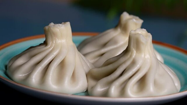 Trio of khinkali dumplings with shiny, soft dough and detailed folds, arranged on a turquoise dish.