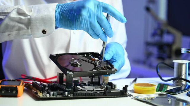 Closeup of technician using screwdriver to fix an open hard drive near a motherboard. and IT services visuals.