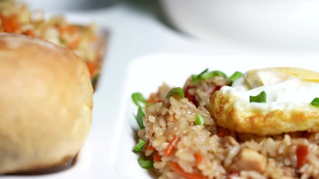 Close-up of fried rice with vegetables, topped with fried egg and served with soft bread.