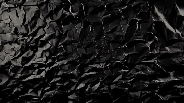 Abstract close-up texture shot of heavily crumpled black paper showing crease lines, providing dramatic graphic element.