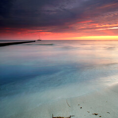 Whispers of the Sea: Vibrant Sunset Casting Golden red Light on Weathered Wooden Groynes