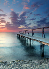 beautiful Vibrant Sunset Casting red Light on Weathered Wooden pier over the sea