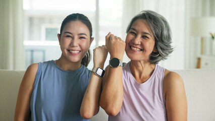 Adult child smile look at camera showing gift AI smart watch IOT app with middle age old mum. Love health care older mom asia elder people sit at home happy wear wrist trace help protect aging life.