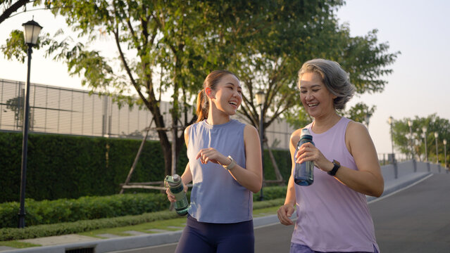 Young adult child workout outdoor public park run walk hold water bottle with mature middle age old mum. Love health care older mom asia elder people happy family protect aging fun joy city life sport