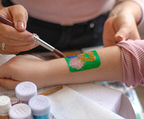 Kid's animator is creating a Shimmering sparkling glitter tattoo on a child's hand at a birthday party. Body art. High quality photo