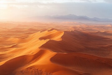 Naklejka premium A vast desert landscape with large golden sand dunes under soft sunlight and hazy mountains in the background, evoking a serene and expansive atmosphere